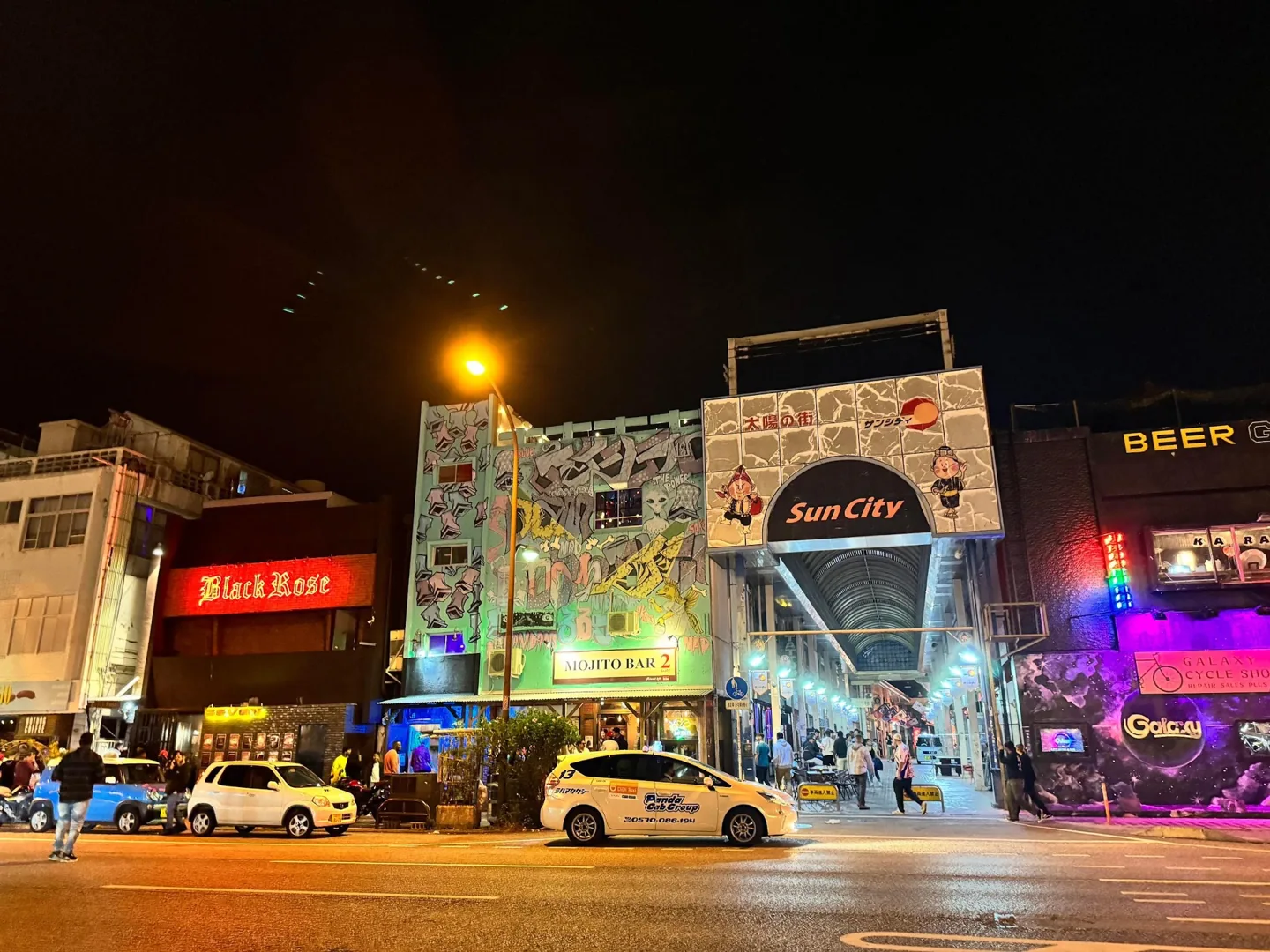 英語看板と壁画が並ぶ夜のサンシティ入口
